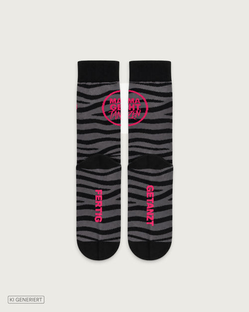 Schwarz-graue Socken mit Zebramuster, pinkem MAMAGEHTTANZEN Logo sowie den Schriftzügen „Fertig“ und „Getanzt“ im Fußbereich